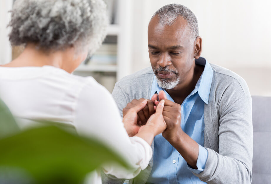 Elderly couple sharing a tender moment while holding hands in a living room.